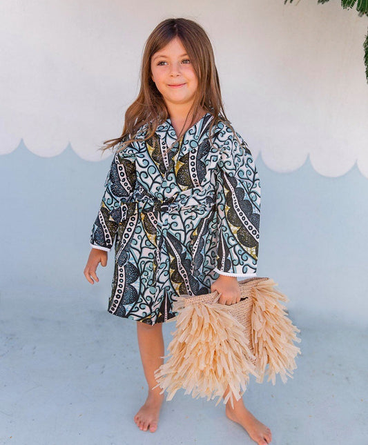 Young girl wearing a patterned dress with a beige skirt against a light blue background